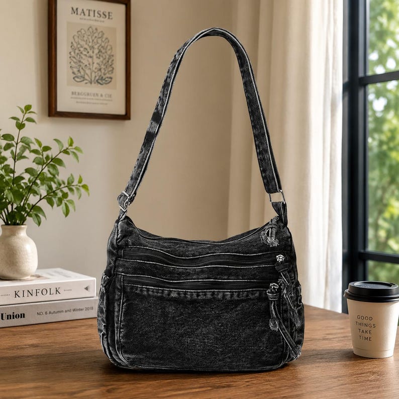 May include: A charcoal gray acid-wash denim shoulder bag featuring multiple exterior zippered compartments, a long adjustable strap, and silver-toned metal hardware. The bag has a structured rectangular base with rounded corners and side pockets.