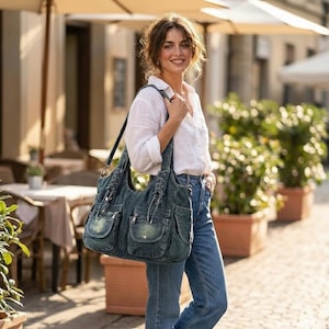 May include: A denim shoulder bag with multiple pockets and a long strap. The bag is a faded blue color and has decorative stitching. The bag is being carried by a person wearing a white shirt and blue jeans.