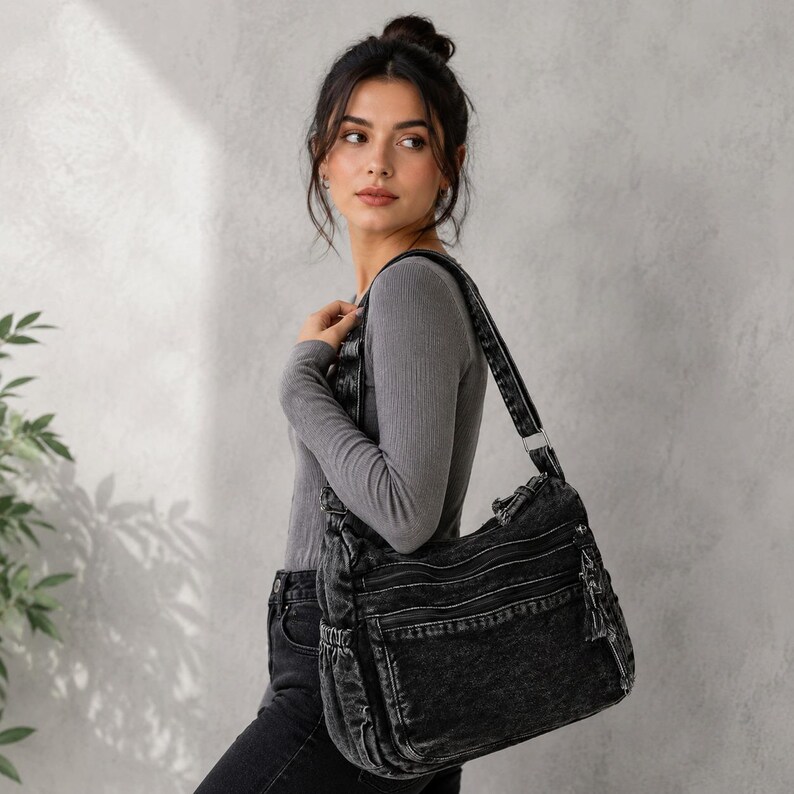 May include: A black acid-wash denim shoulder bag featuring multiple exterior zippered compartments, a wide adjustable strap, and side pockets. The bag has a textured, faded appearance with silver-toned hardware accents and visible zipper pulls.