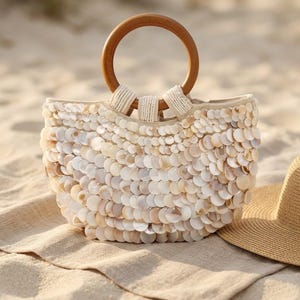 May include: A handbag covered in overlapping iridescent white and cream circular shell discs. The bag features a round, smooth, polished wooden handle attached with white beaded fabric loops. The body of the bag has a curved, semi-circular shape.
