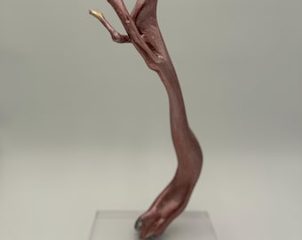 May include: A sculpture titled "Round of Applause" features a stylized, hand-like form in a metallic rose color. The sculpture has gold and silver accents on the fingertips and is mounted on a clear acrylic base.