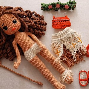 May include: Crocheted doll with brown curly hair, a white diaper, and various accessories. Includes a leaf-shaped paddle, a flower crown, an orange purse, a fringed skirt, a red strap, and red and white sandals. All items are handmade.