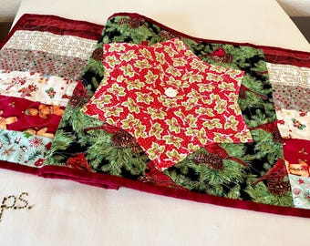 May include: Christmas-themed quilted table runner and star-shaped topper. The runner features stripes with holiday patterns and text, while the topper has a red holly print with a button. The runner is approximately 60 inches long.