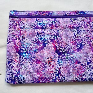 May include: A rectangular fabric pouch featuring a vibrant purple and blue floral pattern with white line-drawn chrysanthemum motifs. The pouch includes a horizontal purple zipper closure across the top and the letters p.s. stitched in black thread.