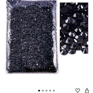 Puede incluir: Una bolsa de pl&aacute;stico transparente llena de numerosas piedras de estr&aacute;s negras, peque&ntilde;as y facetadas. Un primer plano muestra las superficies brillantes y multifac&eacute;ticas de las gemas negras. El color de las piedras de estr&aacute;s es negro.