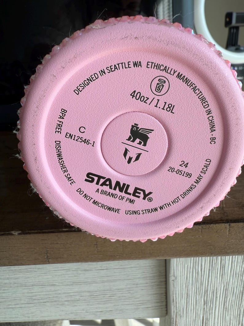 Puede incluir: Primer plano de la base de una botella de agua Stanley rosa. El texto dice "Designed in Seattle WA" y "40oz/1.18L". El logotipo de Stanley est&aacute; en el centro. La botella es libre de BPA y apta para lavavajillas.