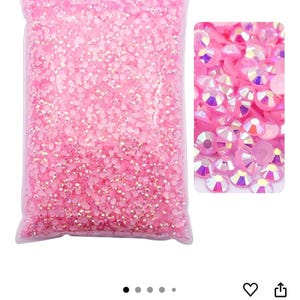 Puede incluir: Una bolsa transparente llena de pedrer&iacute;a rosa claro AB. Un primer plano muestra las facetas iridiscentes de los cristales. El color se describe como Rosa claro AB. Estos pedrer&iacute;a son adecuados para varios proyectos de manualidades.