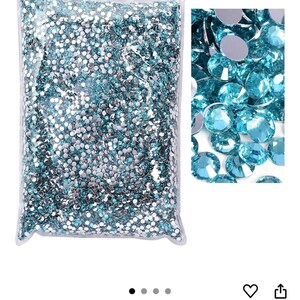 Puede incluir: Una bolsa de pl&aacute;stico transparente llena de pedrer&iacute;a aguamarina. Un primer plano muestra las gemas facetadas, que reflejan la luz. Las piedras de estr&aacute;s son de color azul claro, perfectas para manualidades y adornos.