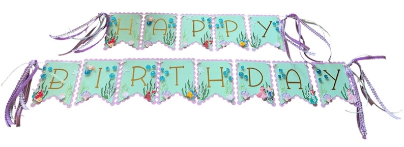 May include: A two-row banner spelling HAPPY BIRTHDAY with light blue scalloped cardstock panels. Each panel features gold lettering, green seaweed illustrations, and small sea creature accents. The banner is strung with purple ribbons.