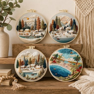 May include: Four circular embroidery hoops featuring detailed landscape scenes. The top left shows a forest campsite, the top right a snowy mountain village, the bottom left a winter cabin scene, and the bottom right a tropical beach with blue water.
