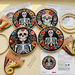 Op de afbeelding: Vier borduur DIY-kunstkits met Day of the Dead schedelontwerpen. Elke kit bevat een zwarte stoffen cirkel met een kleurrijke bloemenkrans en een schedel, omringd door borduurgaren, naalden en instructies.