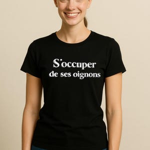 May include: Black t-shirt with the French phrase "S'occuper de ses oignons" in white lettering. The shirt is worn by a person with blue jeans. The phrase translates to "Mind your own business."