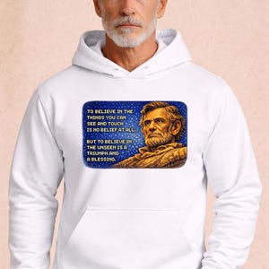 Puede incluir: Sudadera con capucha blanca con un retrato de Abraham Lincoln y una cita sobre la creencia. La imagen está dentro de un rectángulo azul. El texto dice: "Creer en las cosas que puedes ver y tocar no es creer en absoluto... Pero creer en lo invisible es un triunfo y una bendición."