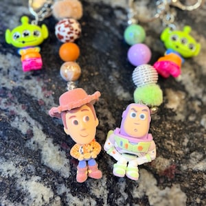 Pu&ograve; includere: Due portachiavi con personaggi del film Toy Story. Un portachiavi ha una figura di Woody e l'altro una figura di Buzz Lightyear. Ogni portachiavi ha una serie di perline colorate e un portachiavi argentato.