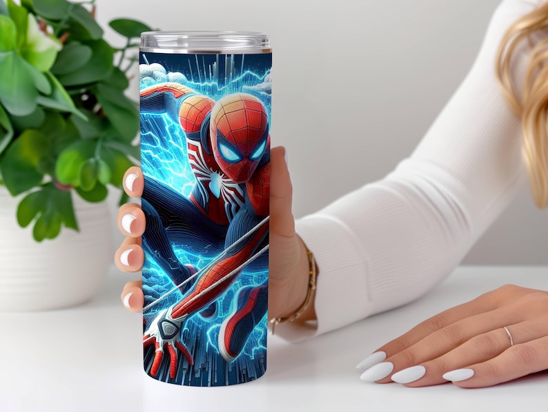 May include: A stainless steel tumbler with a Spider-Man illustration. The design features the superhero in his red and blue suit, set against a backdrop of electric blue energy. The tumbler is held by a person.