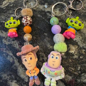 Pu&ograve; includere: Due portachiavi con personaggi del film Toy Story. Un portachiavi ha una figura di Woody e l'altro una figura di Buzz Lightyear. Ogni portachiavi ha perline decorative e un portachiavi argentato.