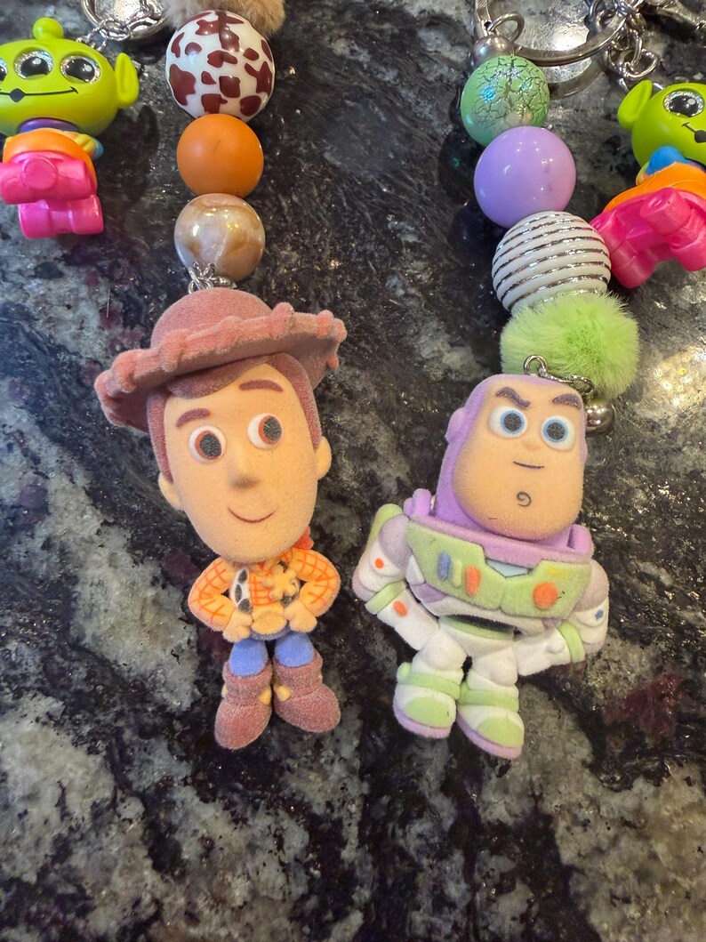 Pu&ograve; includere: Portachiavi con personaggi di Toy Story. I portachiavi includono Woody e Buzz Lightyear, insieme a perline e ciondoli colorati. Il portachiavi di Woody indossa un cappello marrone e il portachiavi di Buzz Lightyear indossa una tuta spaziale.