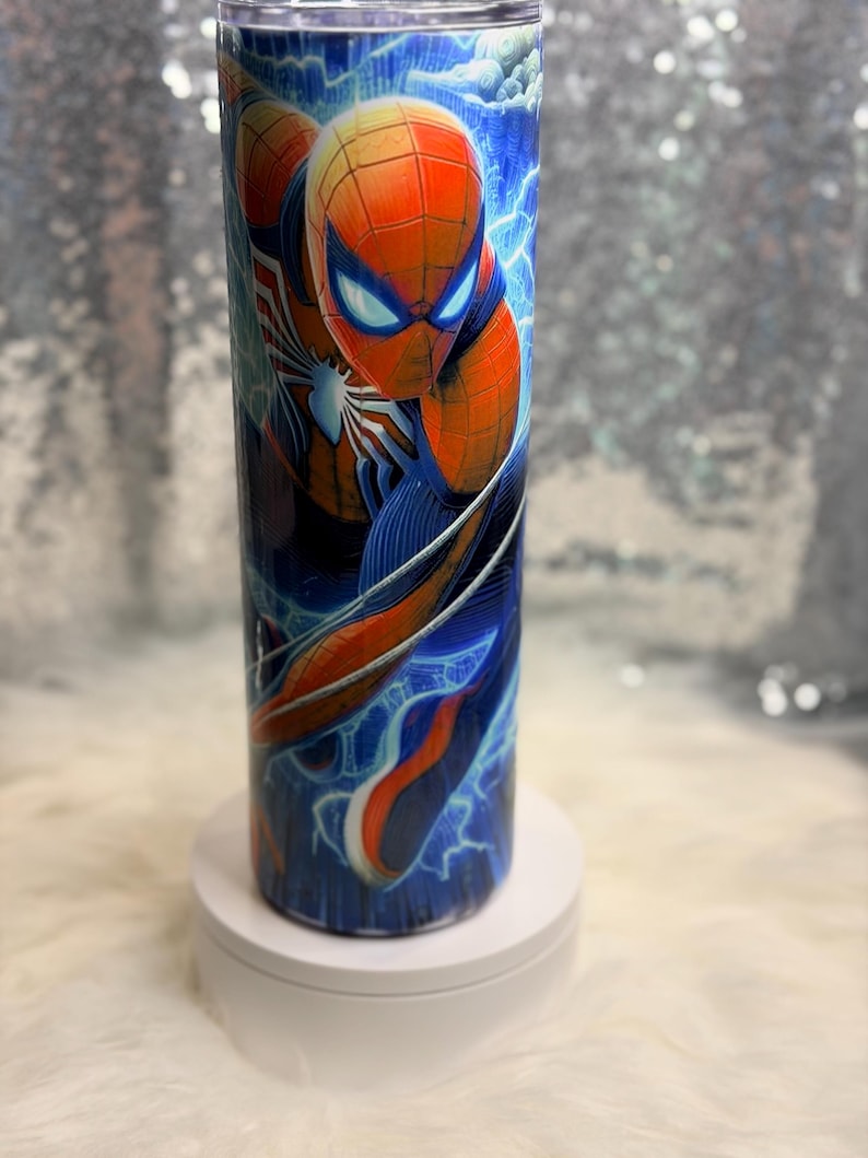 May include: A tall, cylindrical tumbler with a Spider-Man design. The tumbler features the superhero in his red and blue suit, set against a backdrop of blue lightning. The tumbler is likely made of stainless steel, and is approximately 20 cm tall.