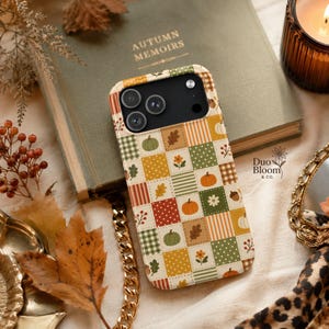 May include: A smartphone case featuring a patchwork design of squares in shades of green, orange, yellow, and white. The pattern includes illustrations of pumpkins, oak leaves, flowers, berries, and various geometric prints like stripes and dots.