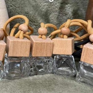 Pu&ograve; includere: Bottiglie di profumo per auto in vetro trasparente con tappi in legno e cordini decorativi. Le bottiglie sono quadrate e hanno una piccola apertura. Alcune hanno una finitura in legno naturale, una &egrave; nera.