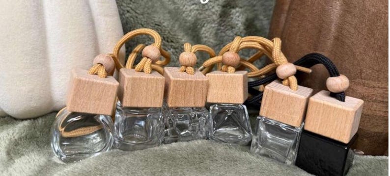 Pu&ograve; includere: Bottiglie di profumo per auto in vetro trasparente con tappi in legno e cordini decorativi. Le bottiglie sono quadrate e hanno una piccola apertura. Alcune hanno una finitura in legno naturale, una &egrave; nera.
