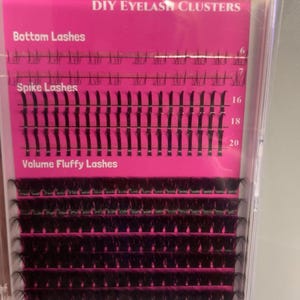 Pode incluir: Uma caixa de plástico transparente contendo clusters de cílios DIY. A inserção rosa exibe o texto "DIY Eyelash Clusters", "Bottom Lashes", "Spike Lashes" e "Volume Fluffy Lashes". Os cílios são pretos e dispostos em fileiras.