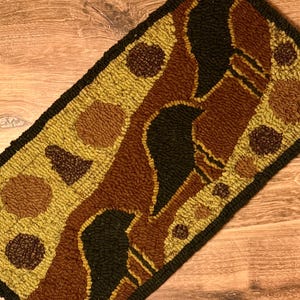 May include: Hand-hooked rug featuring a repeating pattern of black bird silhouettes against a backdrop of brown, tan, and olive green. The rug has a black border and a textured, looped pile. The design is reminiscent of folk art.