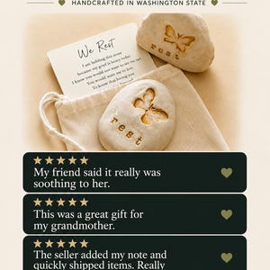 May include: Two smooth, light-colored stones featuring an engraved butterfly and the word "rest," accompanied by a white card with the text "We Rest" and a poem, all placed inside a small, light-colored fabric drawstring pouch.