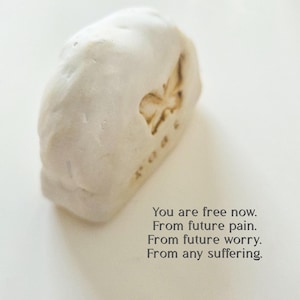 May include: A white, textured, irregular stone-like object featuring an embossed butterfly and the text: You are free now. From future pain. From future worry. From any suffering. The object has a matte finish and a rounded, organic shape.