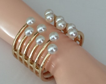 May include: Gold-tone cuff bracelet featuring a series of vertical bars. Each bar is adorned with a white, round pearl. The bracelet is designed to wrap around the wrist, creating a stylish and elegant accessory.