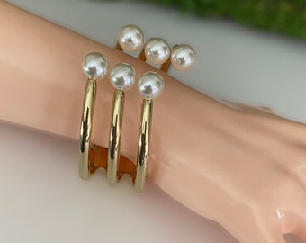 May include: Gold bangle bracelet with three bands and five faux pearl accents.