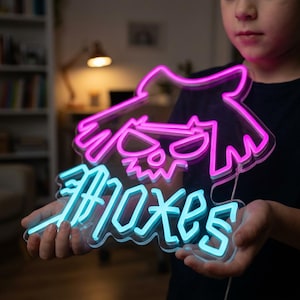May include: A neon sign featuring a cartoon character design with the word "Moxes" in blue neon. The character outline and details are in pink neon. The sign is held by a person.
