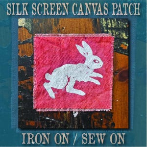 Op de afbeelding: Een vierkante rode canvas patch met een witte zeefdruk van een rennend konijn. De tekst SILK SCREEN CANVAS PATCH en IRON ON / SEW ON is in een schreeflettertype boven en onder de patch op een donkergroenblauwe achtergrond gedrukt.