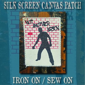 May include: A rectangular canvas patch featuring a black silhouette of a person standing before a pink brick wall graphic. The text "NOT ANOTHER BRICK" is printed in black above the figure. The patch has frayed edges and is designed for iron-on or sew-on application.