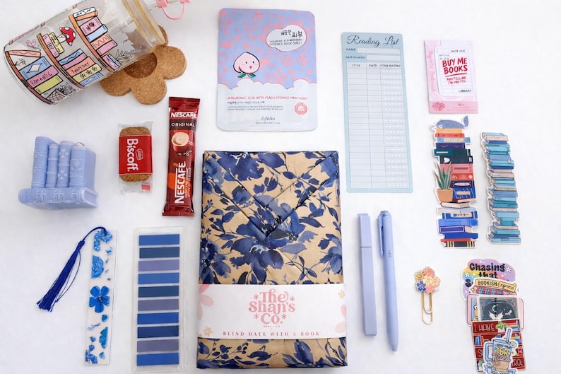 Pu&ograve; includere: Una collezione di articoli a tema librario che include un bicchiere con stampa di libreria, una maschera viso alla pesca, un blocco note per la lista di lettura, un biscotto Biscoff, una bustina di Nescaf&eacute;, una candela blu a forma di libro, un segnalibro floreale, foglietti adesivi, un libro incartato, penne e adesivi.