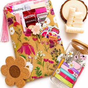 Peut inclure: Une enveloppe à motif floral contenant un sachet de Nescafé, des autocollants et de la papeterie, accompagnée d'un dessous de verre en liège en forme de fleur, d'un verre avec un motif de livres et de fleurs, et de bougies en forme de livres.