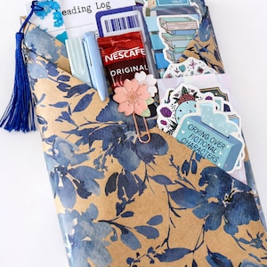 Pu&ograve; includere: Una busta color marrone chiaro con motivo floreale blu contenente un diario di lettura, una nappa blu, due penne azzurre, una bustina di caff&egrave; Nescaf&eacute; Original, una graffetta a forma di fiore rosa e vari adesivi, tra cui uno con scritto Crying Over Fictional Characters.