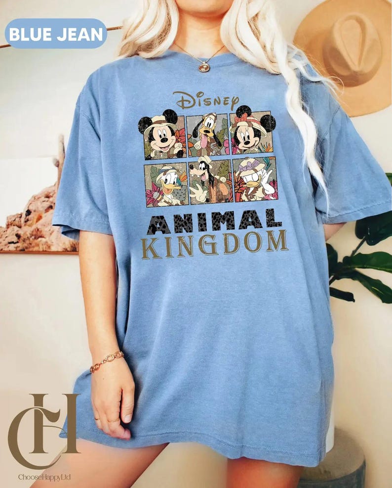 May include: A light blue t-shirt featuring a Disney graphic with Mickey Mouse, Minnie Mouse, Donald Duck, and Goofy. The shirt has the words "Disney Animal Kingdom" printed on the front.