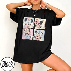 May include: Black t-shirt featuring a colorful graphic of Minnie Mouse in four different poses. Each pose is set within a pastel-colored square. The word "Black" is printed in a white circle at the bottom.