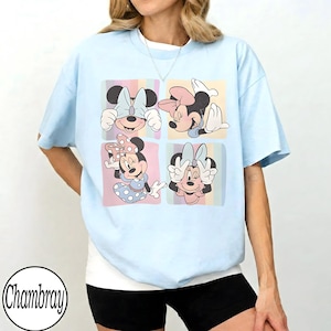 May include: Light blue t-shirt featuring a four-panel graphic of Minnie Mouse in various poses. Each panel has a pastel background. The shirt has short sleeves and a crew neck. The brand name "Chambray" is printed in a circle at the bottom left.