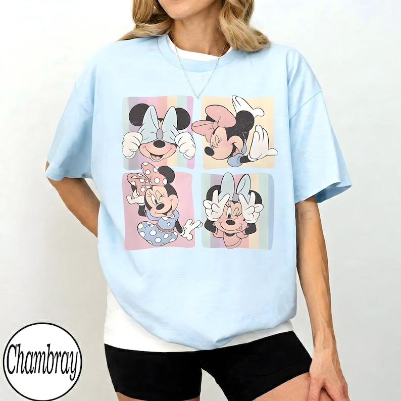 May include: Light blue t-shirt featuring a four-panel graphic of Minnie Mouse in various poses. Each panel has a pastel background. The shirt has short sleeves and a crew neck. The brand name "Chambray" is printed in a circle at the bottom left.