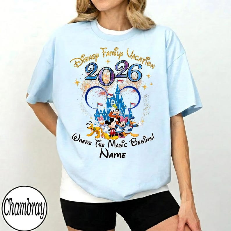May include: Light blue t-shirt with a Disney Family Vacation 2026 graphic. The design features the Disney castle, Mickey Mouse, and friends. The text "Where the Magic Begins!" and "Name" are also included.
