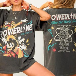 May include: Charcoal grey t-shirt with a Powerline graphic and text. The front shows "POWERLINE" and "WORLD TOUR 45". The back lists cities from the "Stand Out World Tour". A vintage-style graphic tee.