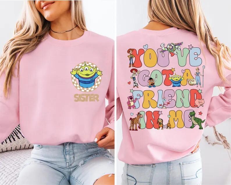 May include: A light pink sweatshirt featuring a cartoon alien with the word "SISTER" below it on the front. The back of the sweatshirt has the phrase "YOU'VE GOT A FRIEND IN ME" with various cartoon characters.