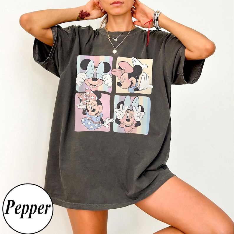 May include: Dark grey t-shirt with a four-panel graphic of Minnie Mouse in different poses. Each panel has a pastel background. The shirt has short sleeves and a relaxed fit. The word "Pepper" is in a white circle at the bottom.