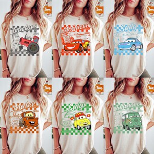 May include: Cream-colored t-shirts featuring various cartoon car characters and the text "Tractors", "McQueen", "Sally", "Mater", "Luigi", and "Fillmore". Each design includes the year "2006" and a checkered background.