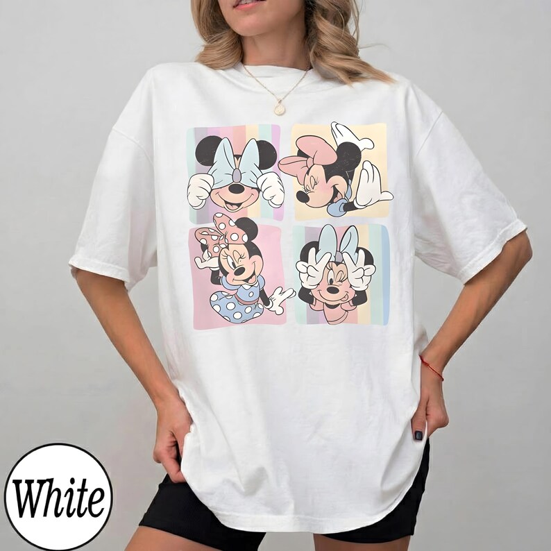 May include: White t-shirt featuring a colorful graphic of Minnie Mouse in four different poses. Each pose is set against a pastel-colored background. The shirt has a relaxed fit and short sleeves.