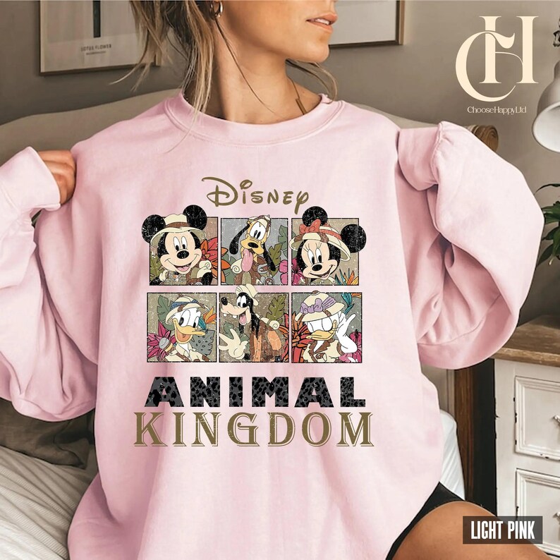 May include: Light pink sweatshirt featuring Disney characters Mickey Mouse, Minnie Mouse, Donald Duck, and Goofy. The design includes the word "Disney" above the characters and "Animal Kingdom" below. The sweatshirt is a crew neck style.