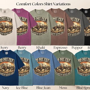 May include: A collection of Comfort Colors t-shirts in various colors, each featuring a graphic with a bison and the text "DO NOT PET THE FLUFFY COWS" and "Yellowstone National Park EST. 1872". Colors include ivory, berry, khaki, espresso, pepper, black, navy, ice blue, blue jean, moss, and blue spruce.