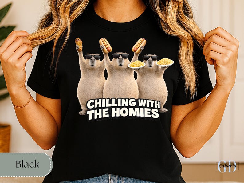 K&ouml;nnte beinhalten: Schwarzes T-Shirt mit einer Grafik von drei Capybaras, die Sonnenbrillen tragen und Essen halten. Der Text "CHILLING WITH THE HOMIES" ist darunter aufgedruckt. Die Capybaras halten einen Hotdog, einen Maiskolben und einen Teller Pasta.